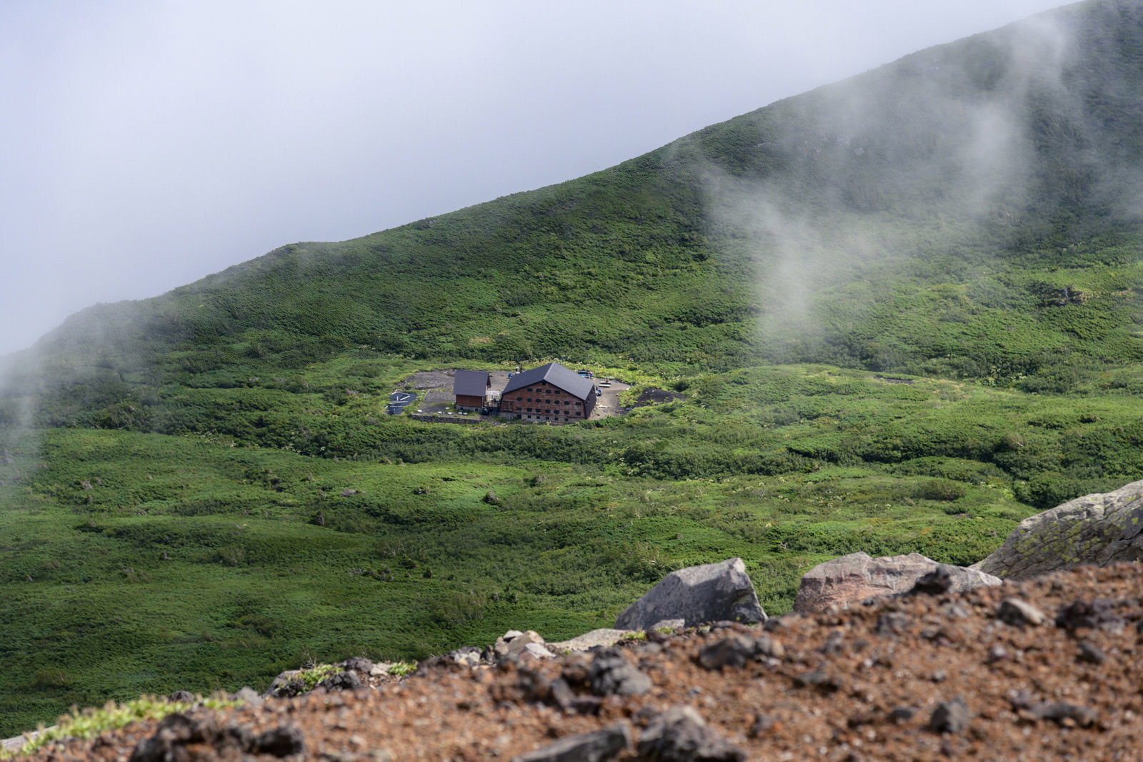 霧に包まれた緑の山肌に建つ山小屋の風景