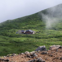雲の向こうに見える岩手山8合目の山小屋と緑の山肌の写真