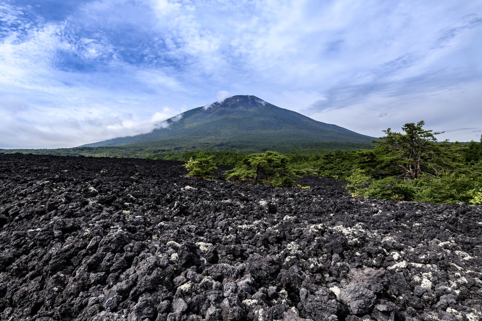 青空を背景に黒い溶岩の岩肌が特徴的な岩手山を麓から見上げた風景