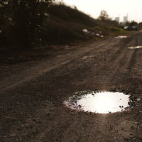 夕日を反射する農道の砂利道にできた水たまりの写真