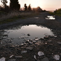 朝日を待つ砂利道に映る水溜りの空と小石の風景の写真