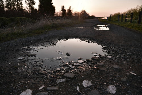 朝日を待つ砂利道に映る水溜りの空と小石の風景