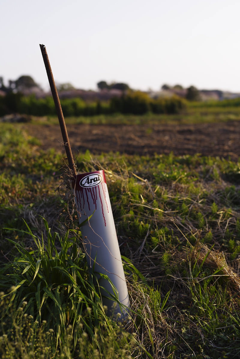 畑脇に立つ農具を入れる白い筒と錆びた金属の棒