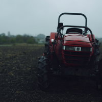 雨に濡れる赤い農業用トラクターが停車する畑の写真