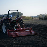 畑を耕す使い古された赤いロータリー付きトラクターの写真