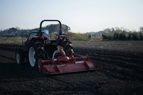 畑を耕す使い古された赤いロータリー付きトラクター