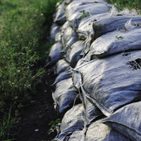草が生えた積み上げられた砂袋と防水シートの写真