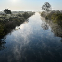 朝靄と湯気が沸き立つ穏やかな川の水面に映る朝空の写真