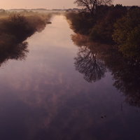 紫色に染まる朝の川と空、靄が立ちのぼる水面の写真