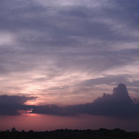 街に沈みゆく夕日と薄紫の曇り空の写真