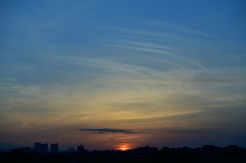 オレンジ色の夕空に細く伸びる飛行機雲と夕日