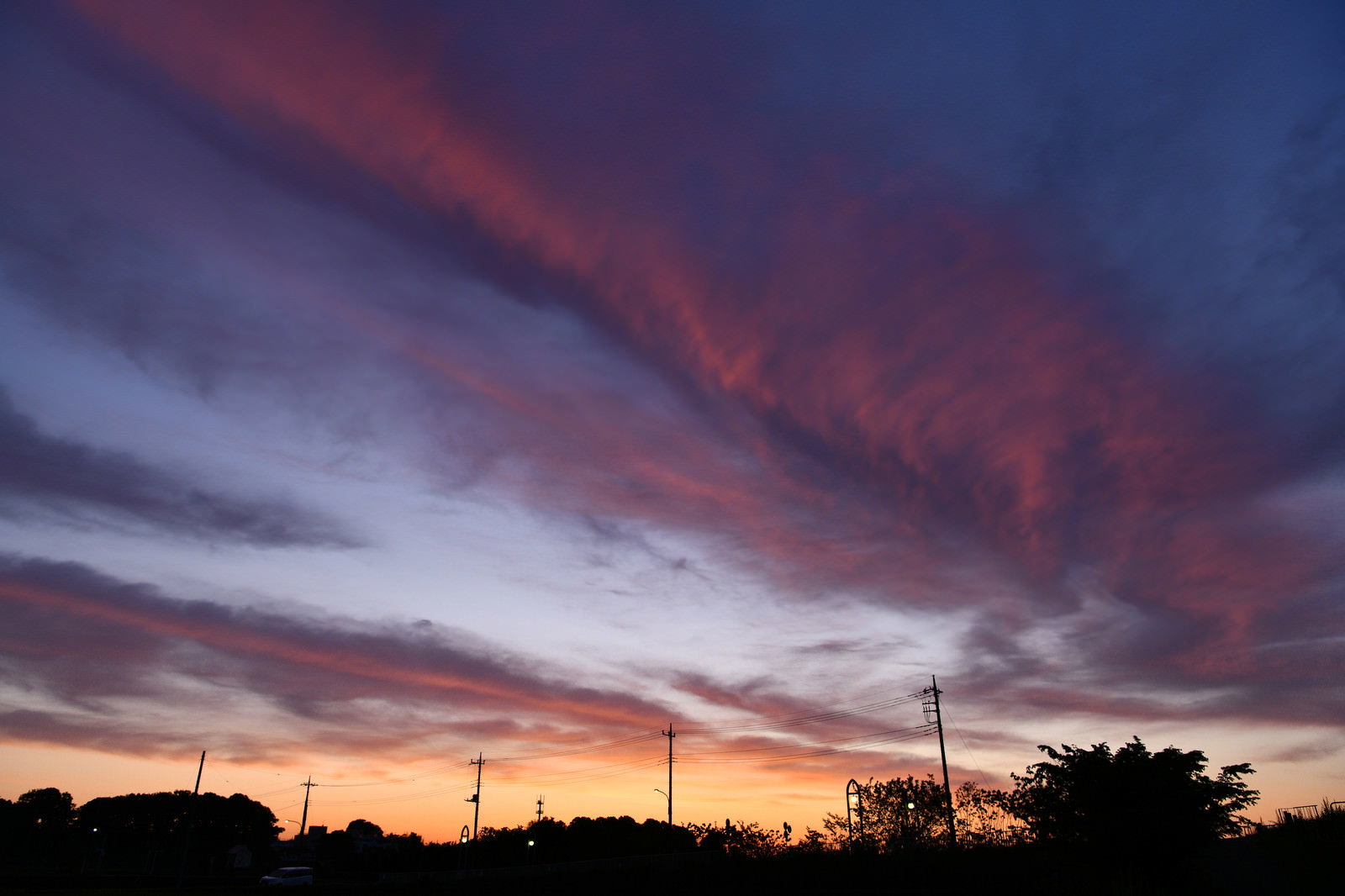 朝焼けに染まった雲と空、地平線に木々のシルエット