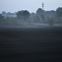 朝霧の中、農地の奥に立つ鉄塔と電線が描く風景の写真