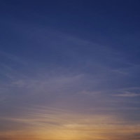 深く青い空に沈むオレンジ色の夕日と山々のシルエットの写真