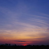 薄い幕が重なるような空と夕日、地平線に沈む太陽の写真