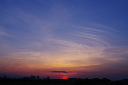 薄い幕が重なるような空と夕日、地平線に沈む太陽