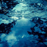 梅雨時期の水溜りに映り込む青い空と白い雲の写真