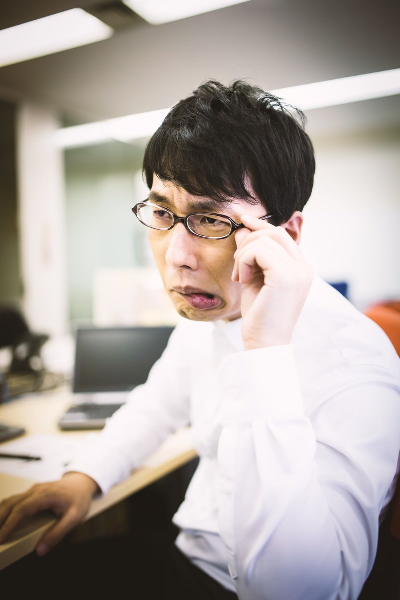 オフィスで眼鏡を直し口をへの字に結ぶ男性会社員［モデル：大川竜弥］