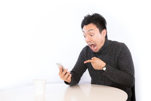 スマートフォンの画面を見てまさかの高額当選に驚く男性
