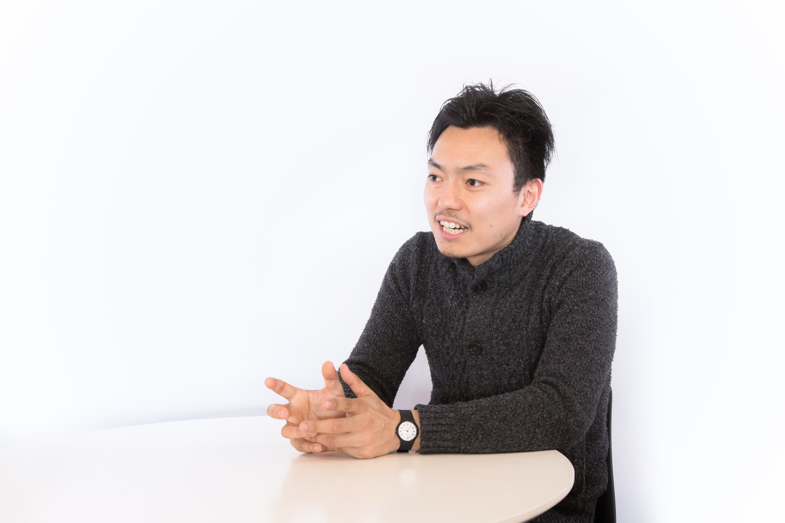 テーブルで両手を組みインタビューに答える男性