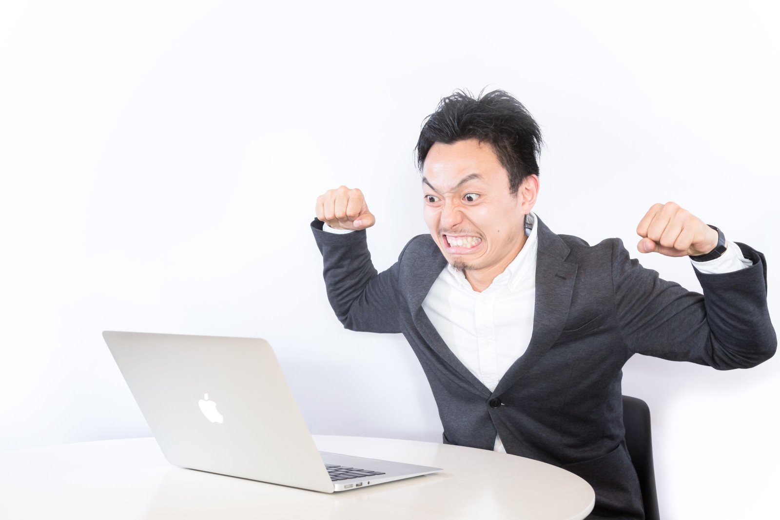 パソコン前で拳を作り怒るスーツ姿の男性［モデル：藤沢篤］