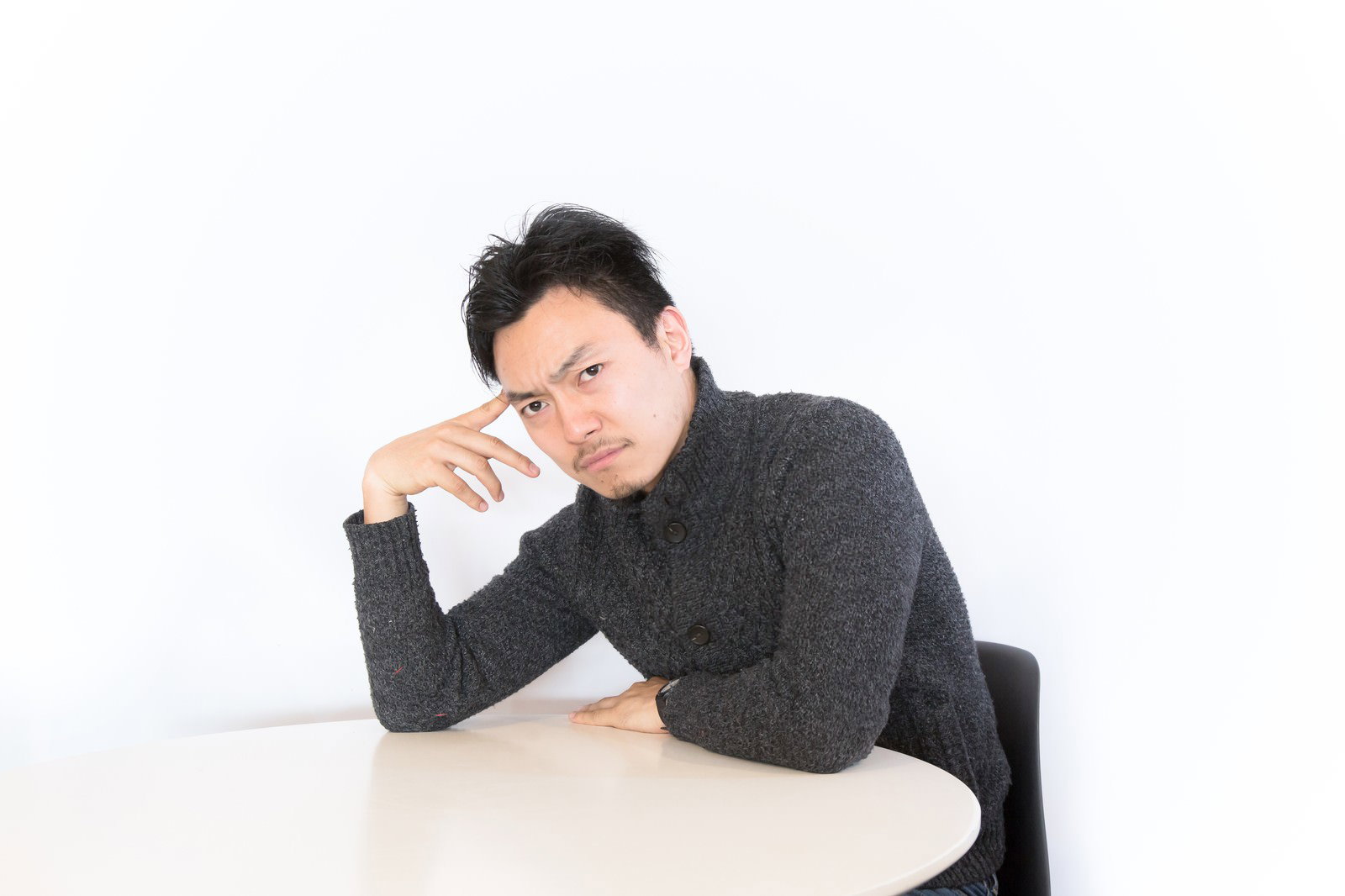 頬杖をつき不機嫌な表情で向き合う男性［モデル：藤沢篤］