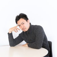 テーブルに頬杖をついて上から目線で相談に乗る男性の写真