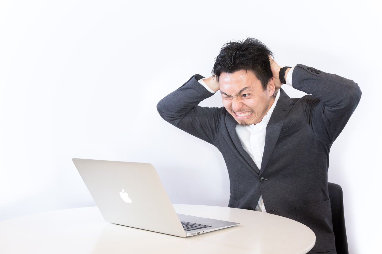 スーツの男性がデスクで頭を抱えて悩む［モデル：藤沢篤］