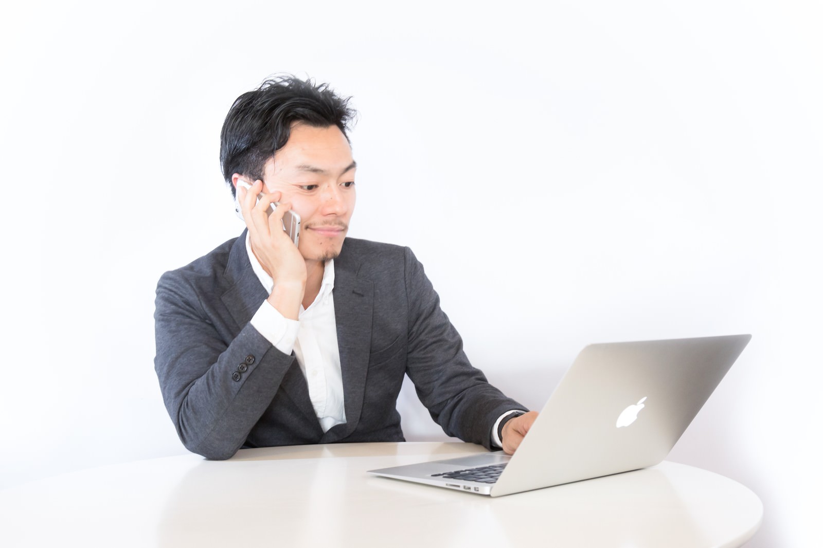 ノートパソコンで作業しながら通話するビジネスマン［モデル：藤沢篤］