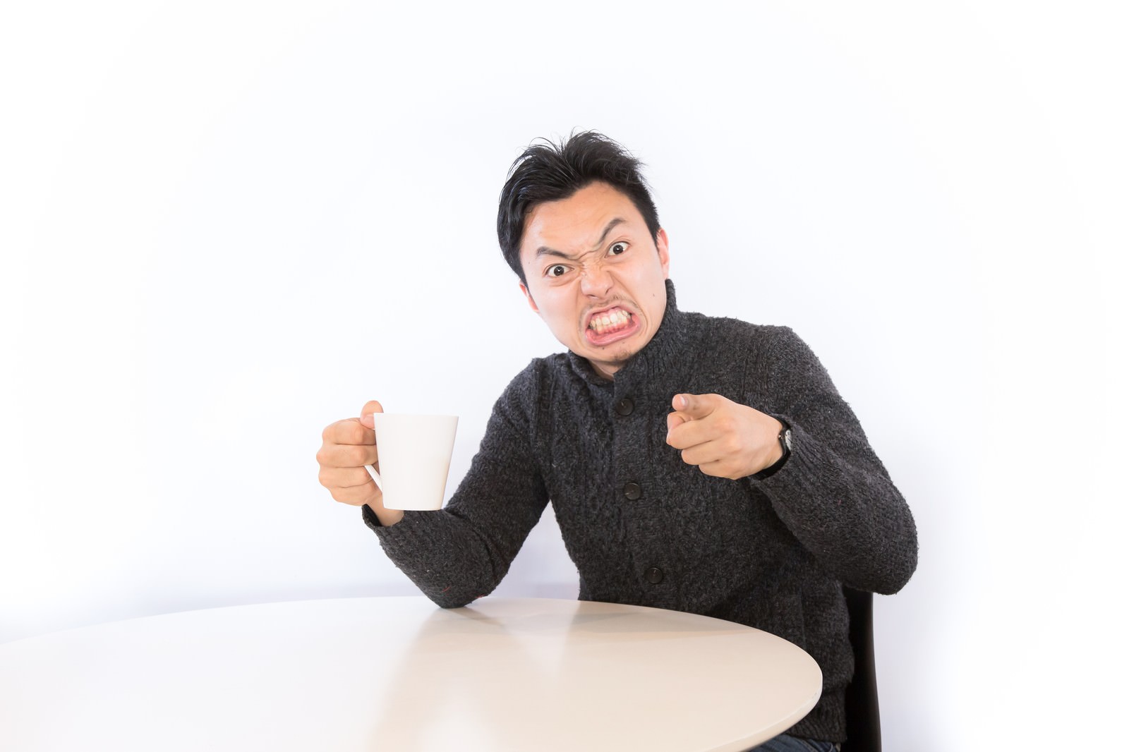 マグカップを持ち指を突きつけて怒る男性［モデル：藤沢篤］