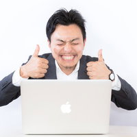 結果オーライ！ノートパソコン前で両手サムズアップを決めるスーツ姿の男性の写真