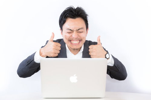 結果オーライ！ノートパソコン前で両手サムズアップを決めるスーツ姿の男性