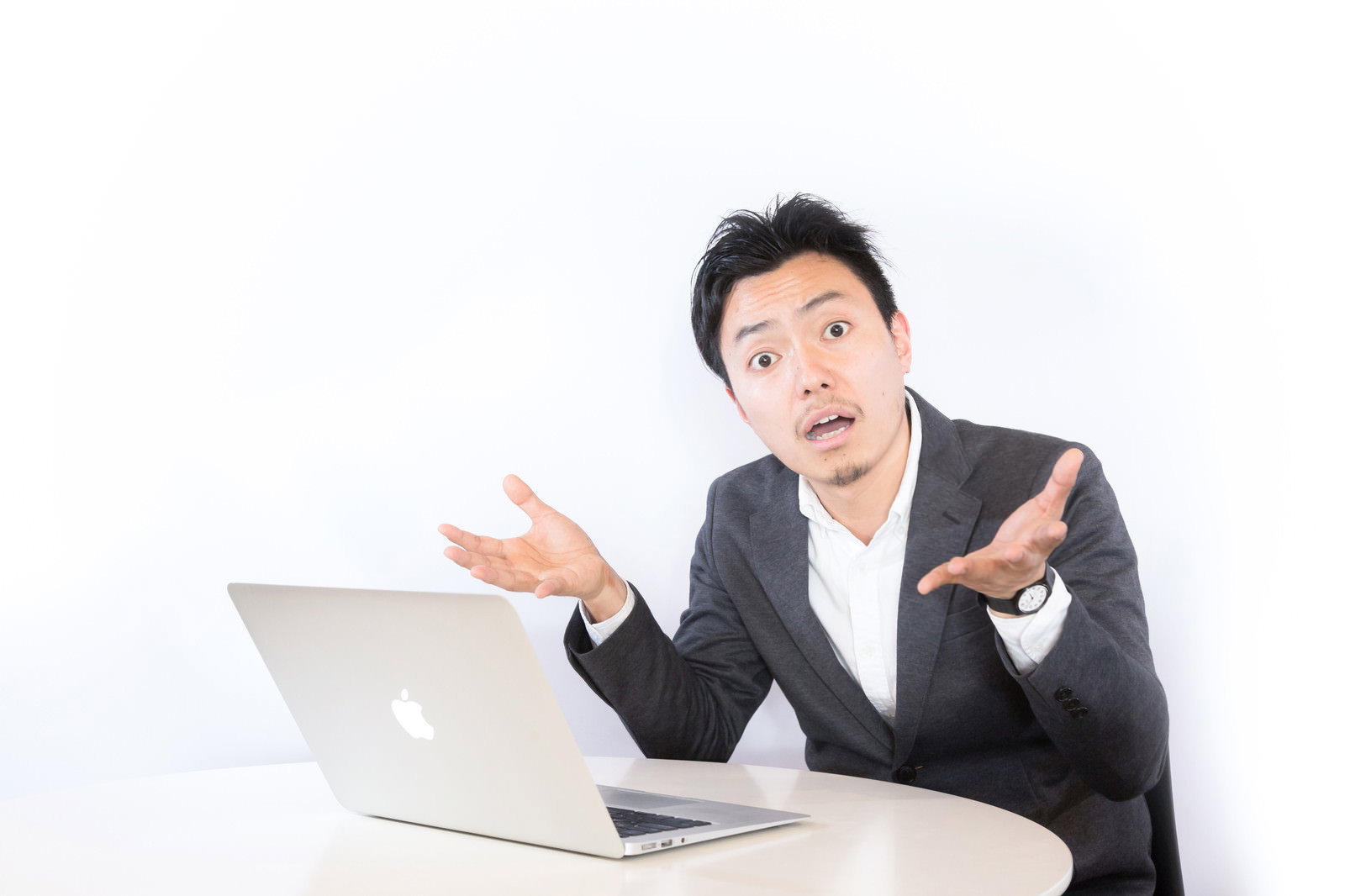 ノートパソコンの前で両手を広げて呆れる男性［モデル：藤沢篤］