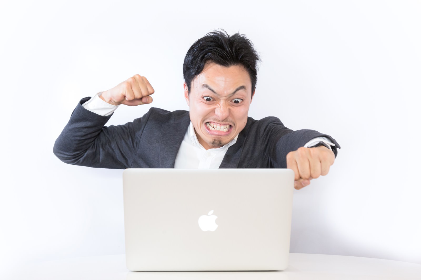ノートパソコンの前で拳を握り怒るスーツ姿の男性［モデル：藤沢篤］
