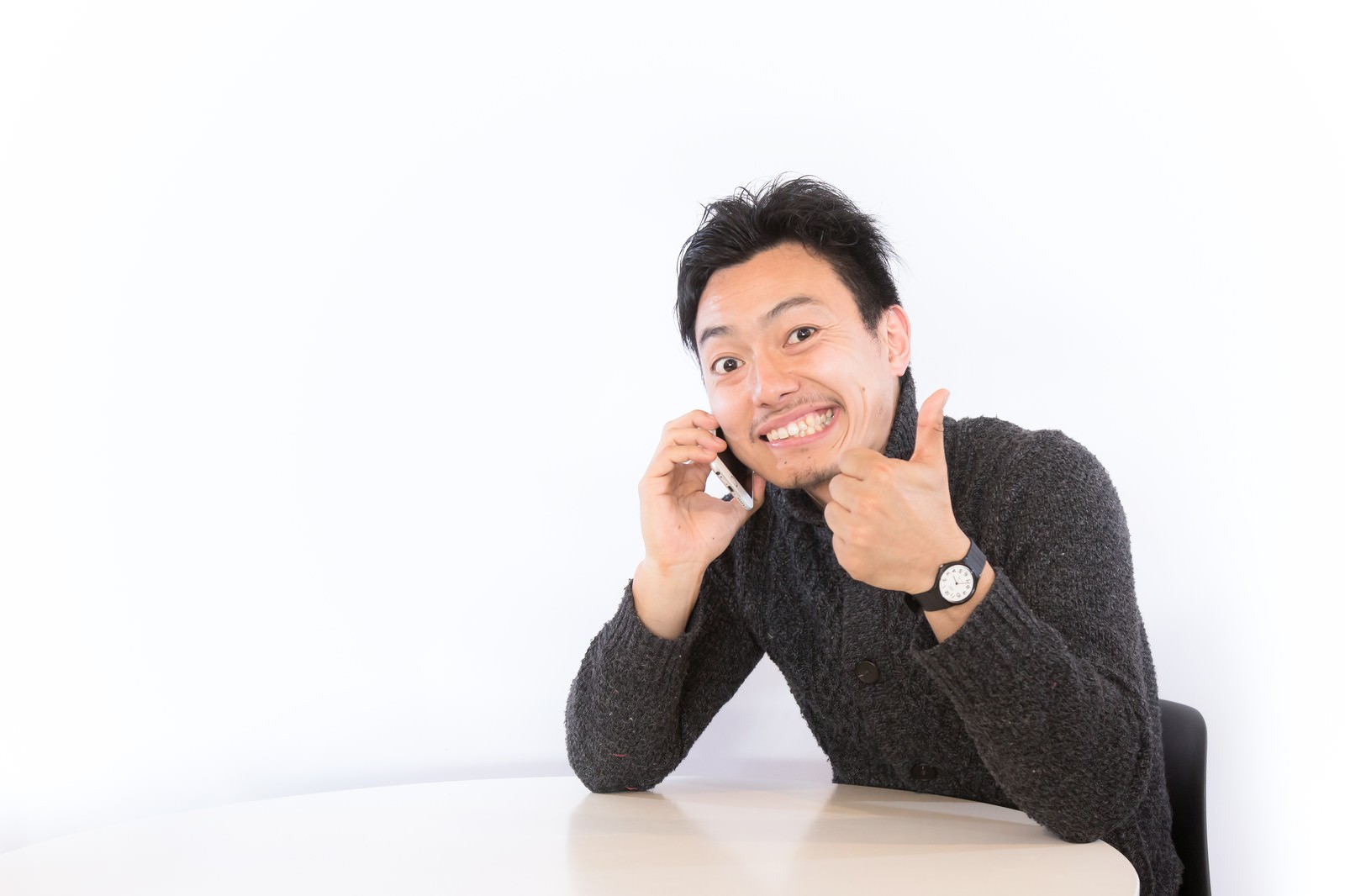 スマホを持ち親指を立てるサムズアップポーズの男性［モデル：藤沢篤］