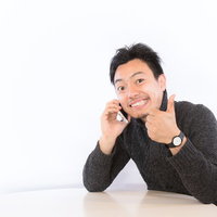 スマホを持ってサムズアップする男性のビジネスポーズの写真