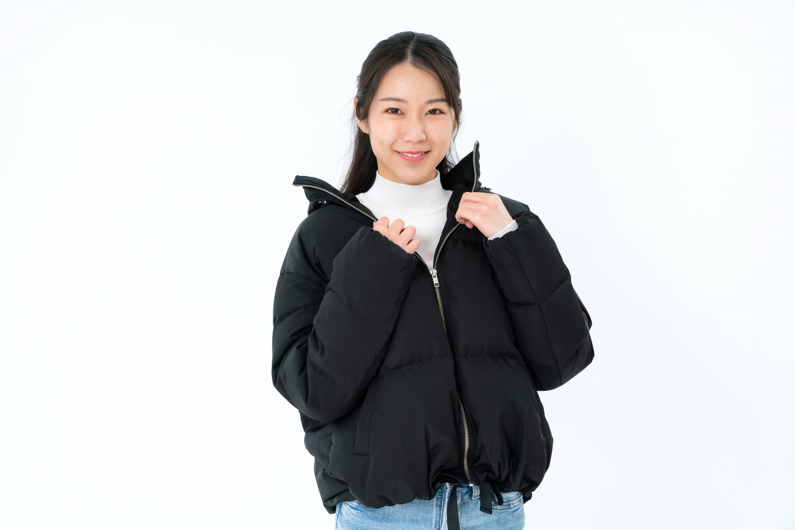 白い背景で黒いダウンジャケットを羽織りながら笑顔を見せる女性［モデル：SAKI］