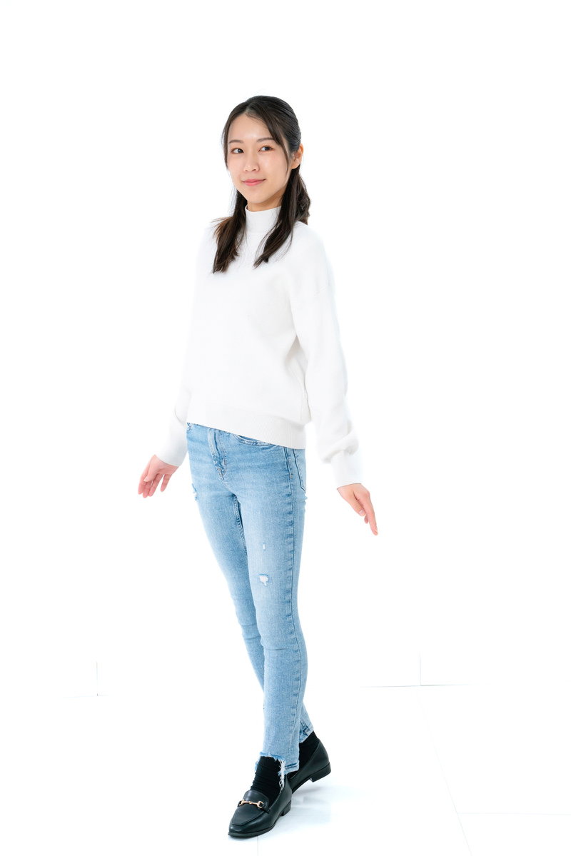 白いトップスとデニムパンツを着用した女性が白背景で全身ポーズをとっている［モデル：SAKI］