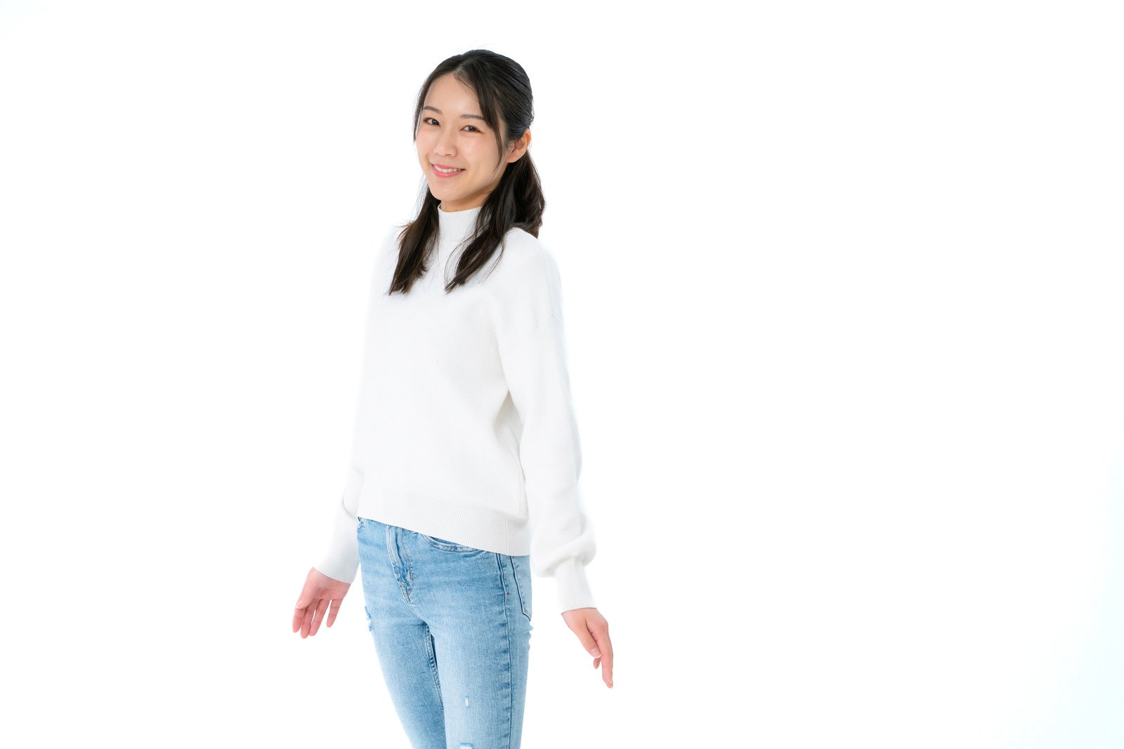 白いトップスとデニムを着て白い背景で微笑む女性［モデル：SAKI］