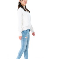 白いトップスとジーンズで背筋を伸ばして立つ女性の写真