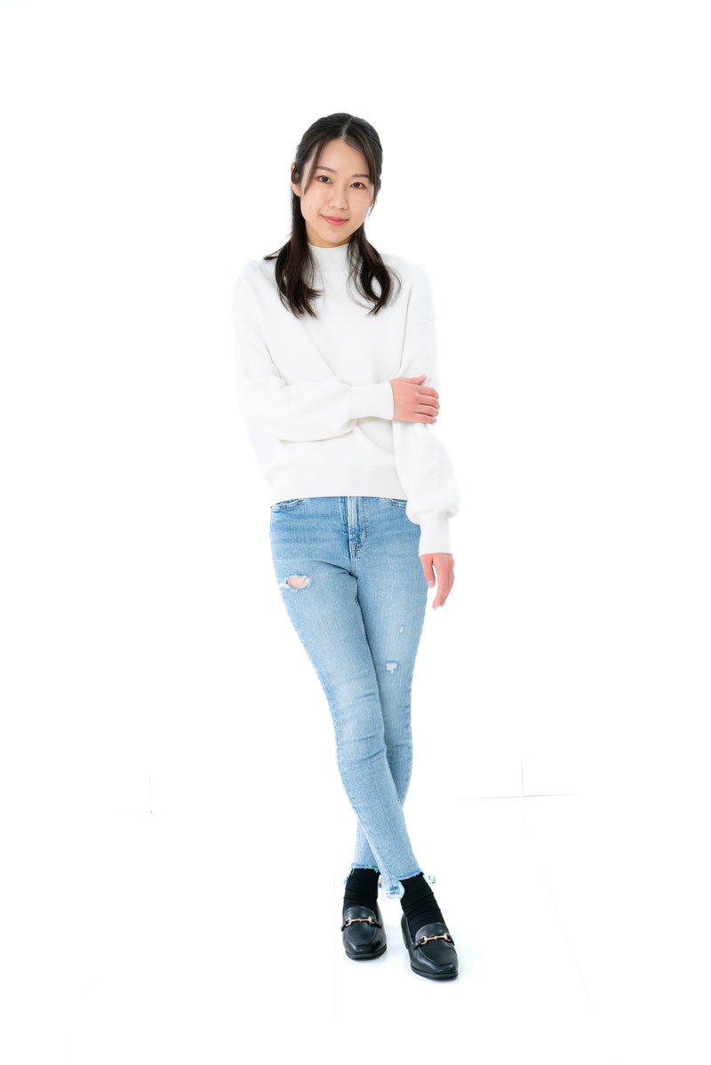 白背景で足を交差して腕を組み、恥ずかしそうにポージングする女性［モデル：SAKI］