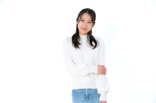 左腕をおさえて微笑む女性のポーズ、白トップスとデニム姿