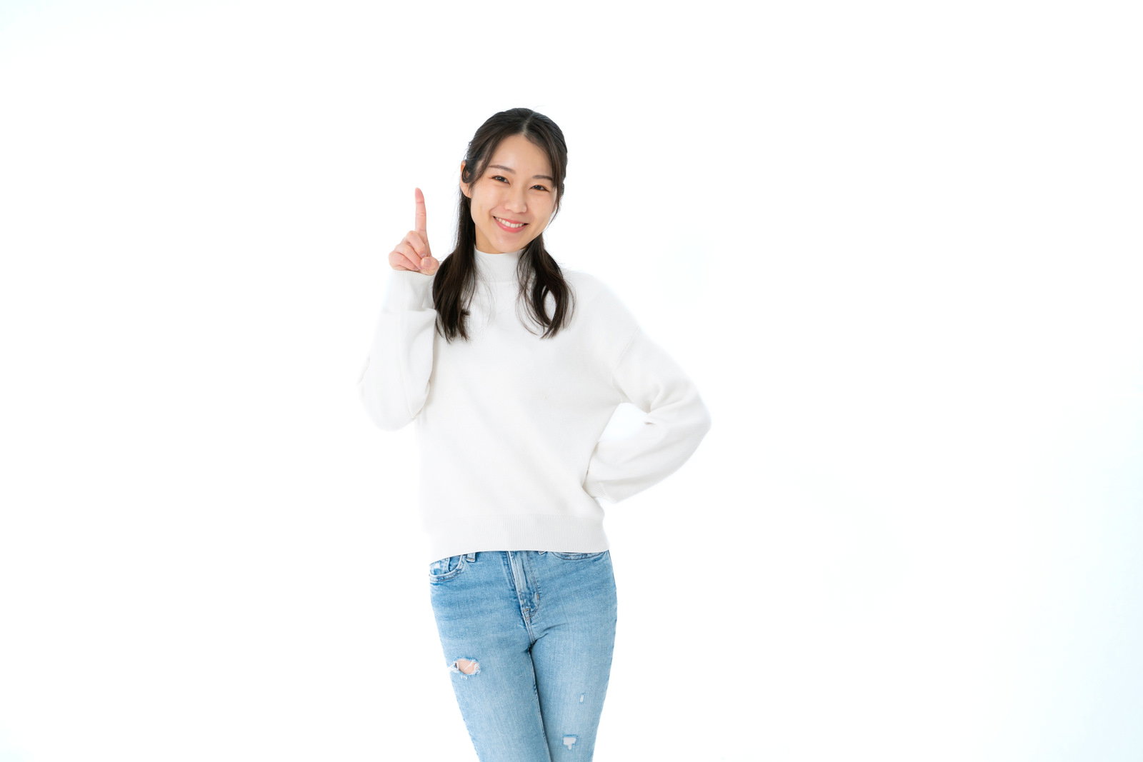 白背景で人差し指を上に向けて笑顔でポーズを取る白いトップスの女性［モデル：SAKI］