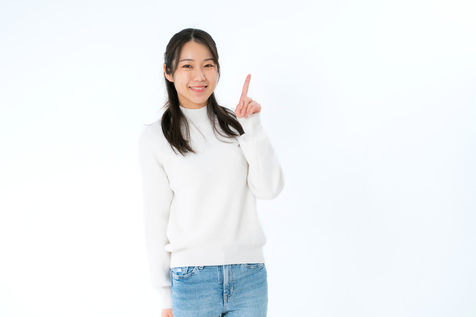 白背景で微笑みながら人差し指を立ててアピールポーズをする女性［モデル：SAKI］