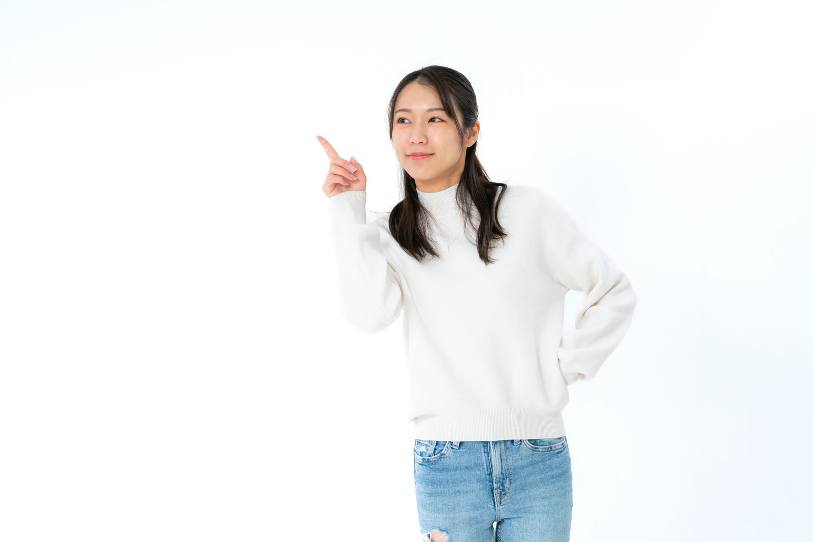 白いニットを着た女性が人差し指で右方向を指しながら微笑んでいる［モデル：SAKI］