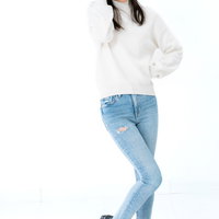 白ニットとジーンズ姿で足をくねらせて困惑する女性のポーズの写真