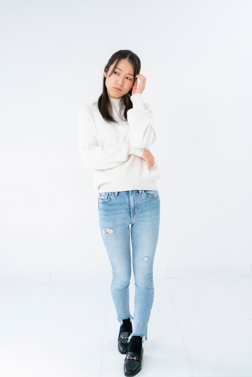 白いセーターを着た立ち上がって頭を抱える悩む女性のポーズ