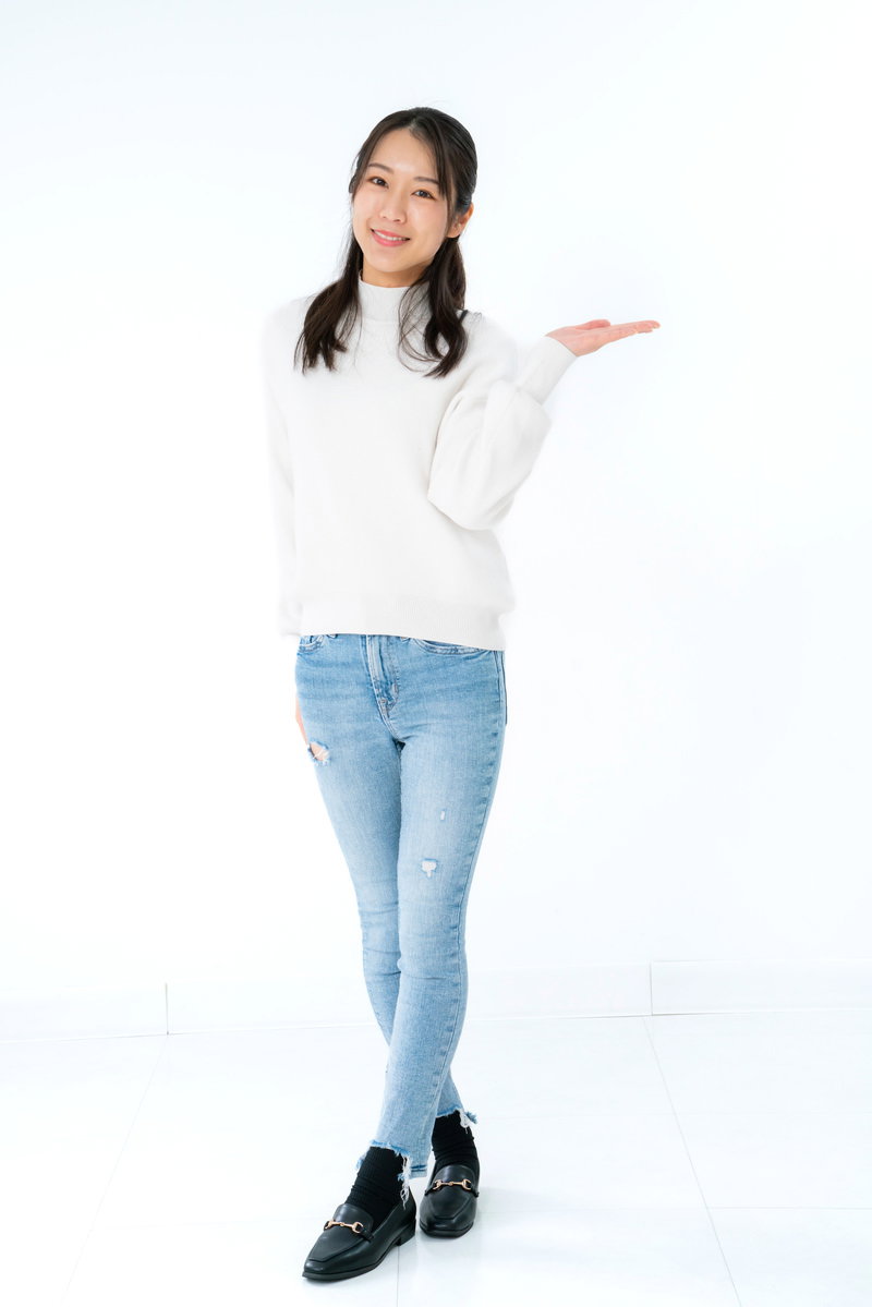 左手を広げてこちらを見ながら微笑む白いニット姿の女性［モデル：SAKI］