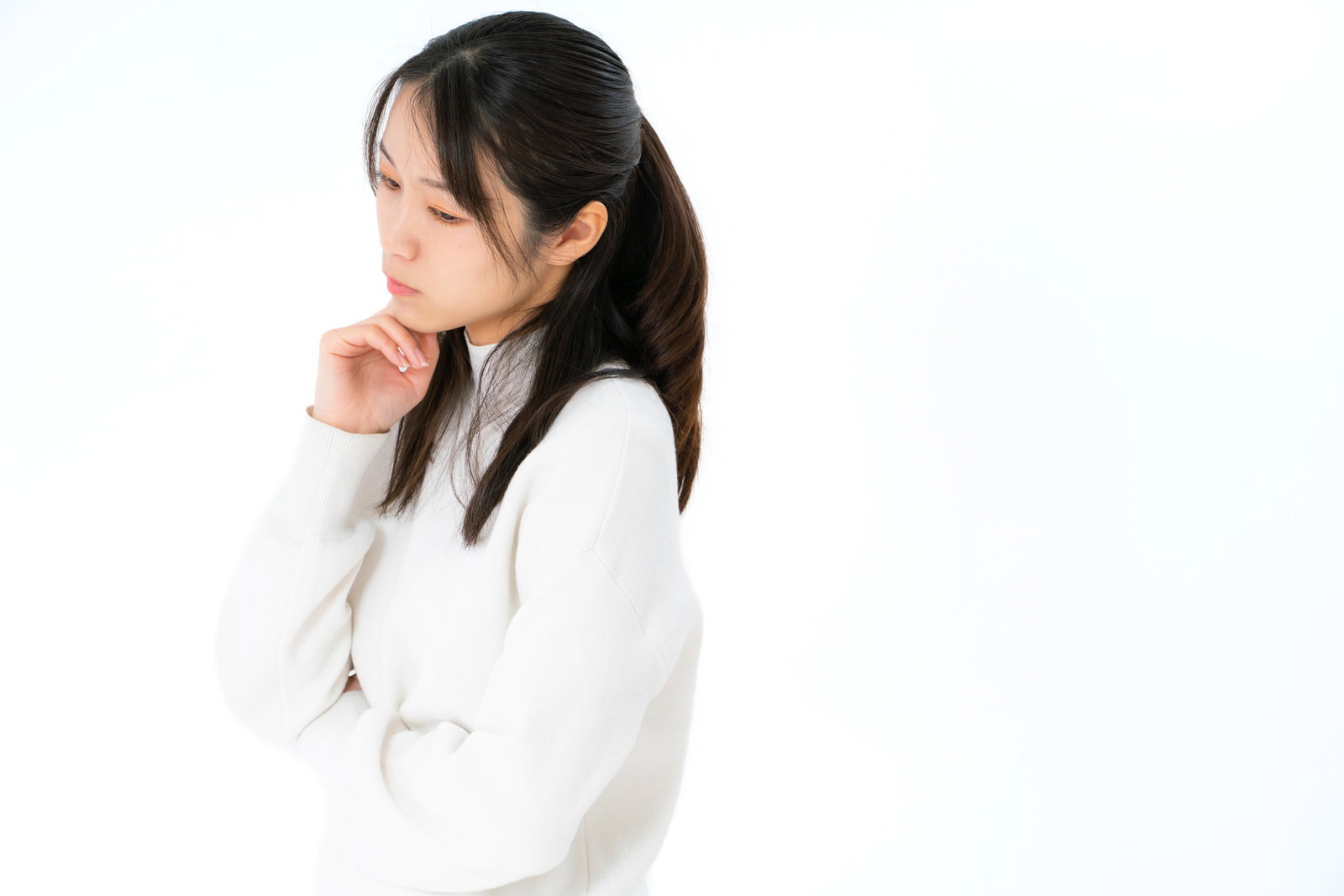 白い服を着た女性が手を顎に当てて考え事をしている様子［モデル：SAKI］