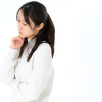 白背景で手を顎に当てて考え事をする女性のポートレートの写真